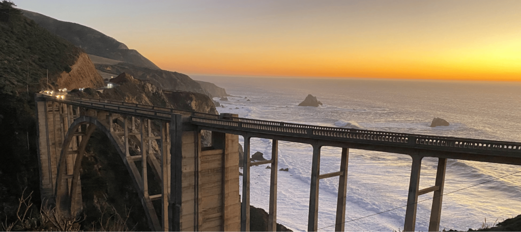 image at sunset with the waves crashing against the beach with a bridge connecting two bluffs
