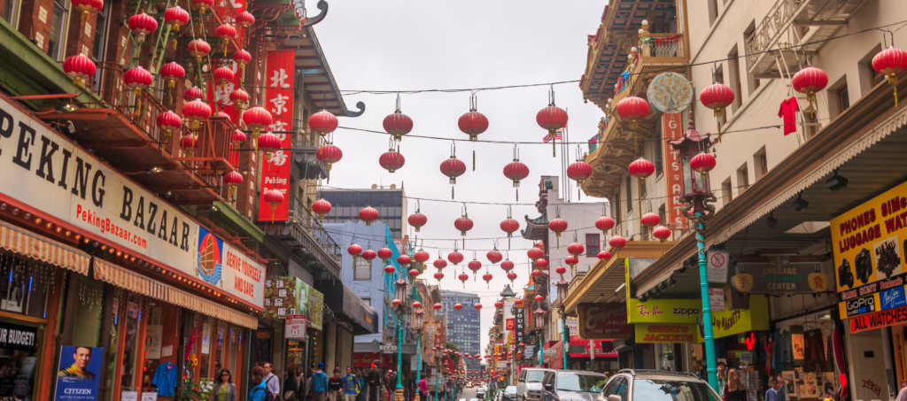 a street in chinatown where you see lots of signs of local businesses and chinese lanterns strung from side to side