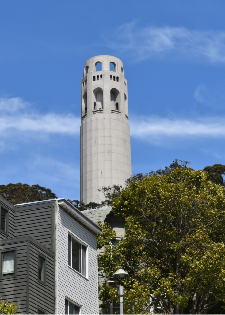 a stone tower, coit tower, in the background with a home and tree in the foreground
